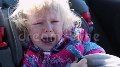 白种人小女孩，卷发，穿着温暖的夹克，坐在儿童座椅上，戴着安全带坐在车上